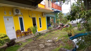 A yellow building with a balcony, a small garden with a pond, and a parked motorcycle. - Malompek (Padang)
