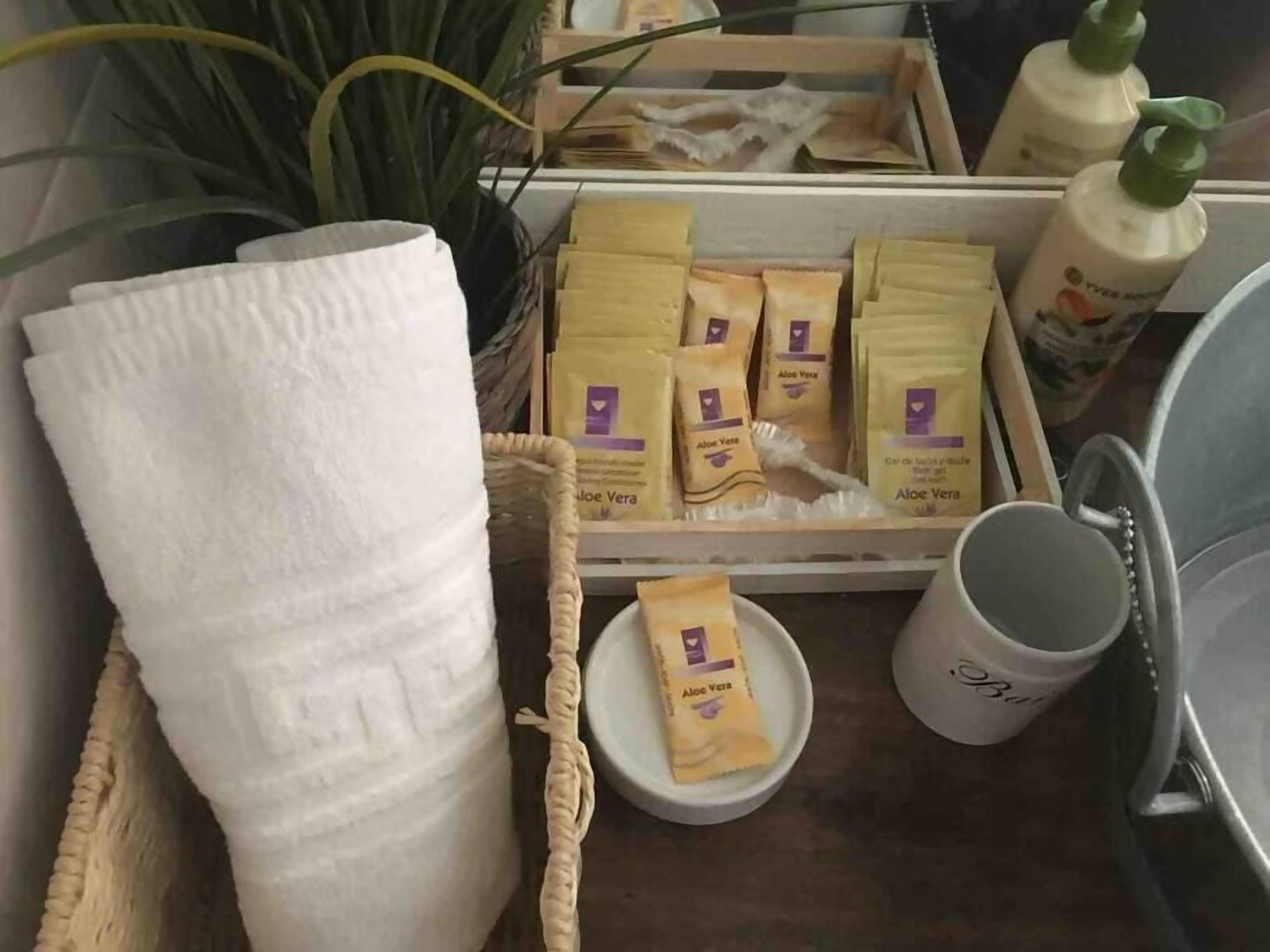 Una bandeja con una toalla blanca, sobres de aloe vera, un cuenco pequeño con aloe vera y una taza.