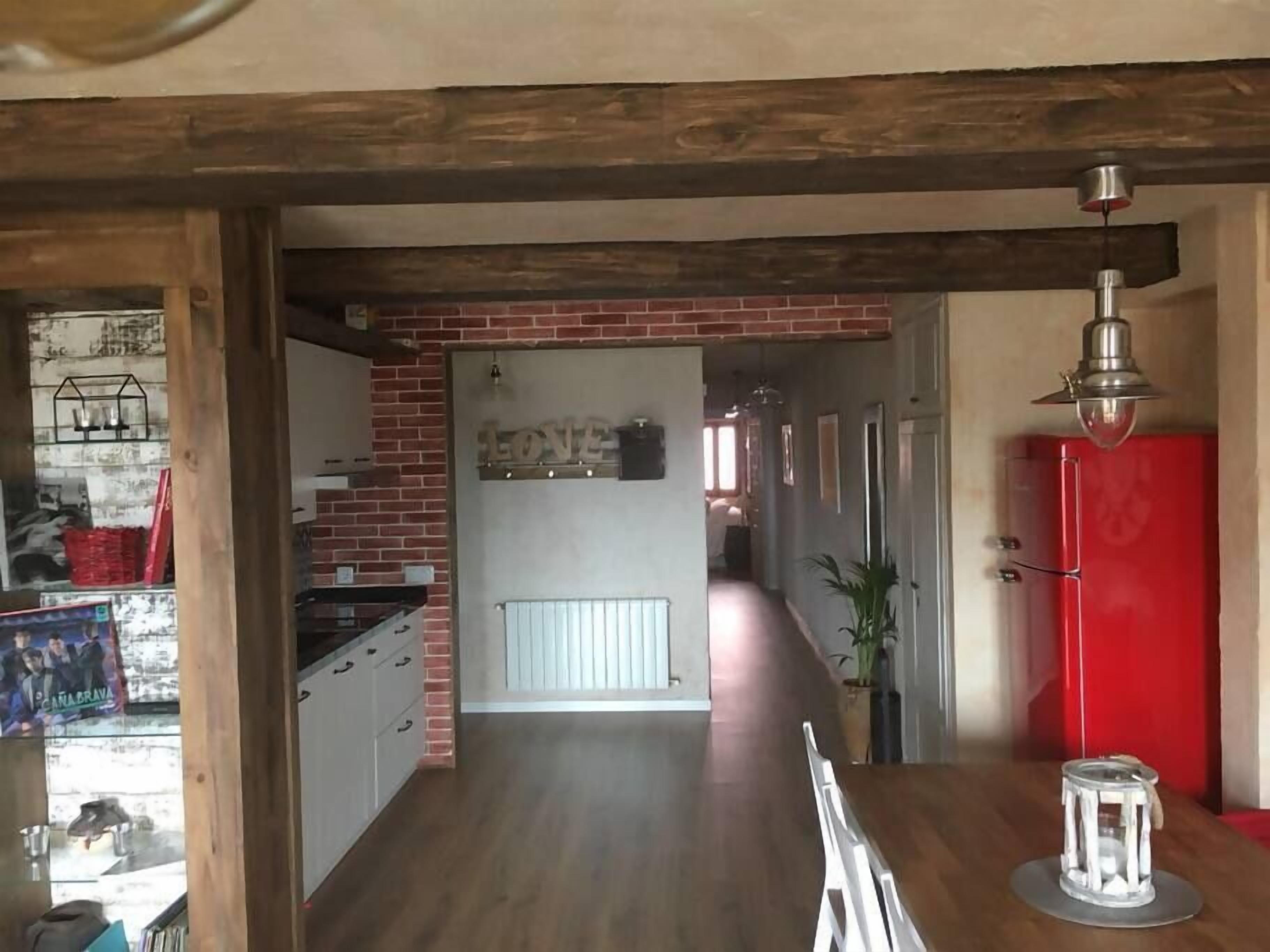Una cocina con pared de ladrillo, vigas de madera en el techo y un refrigerador rojo.