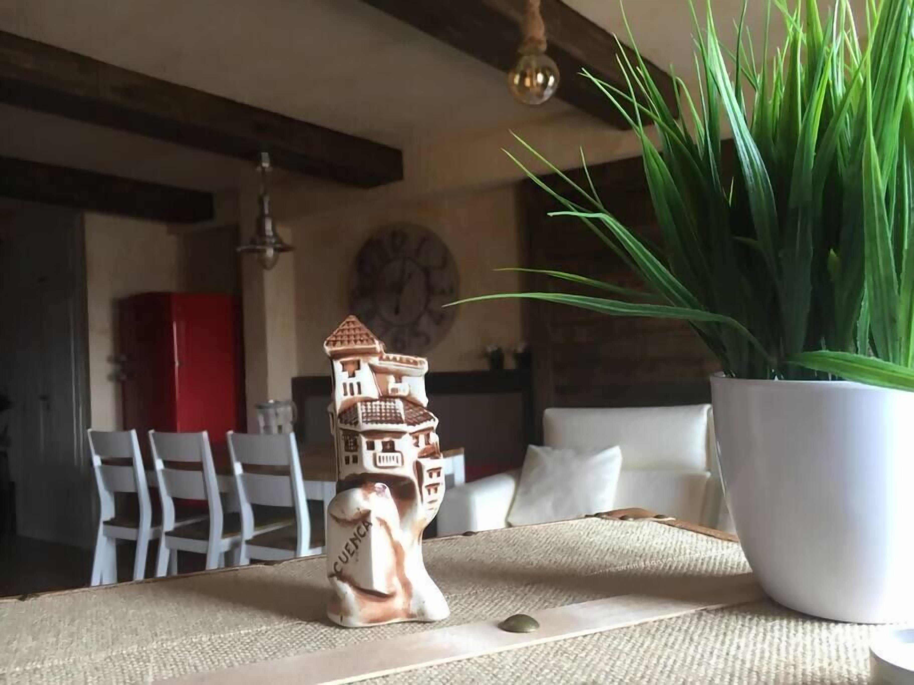 A dining table with a ceramic house figurine, a potted plant, and a clock on the wall.