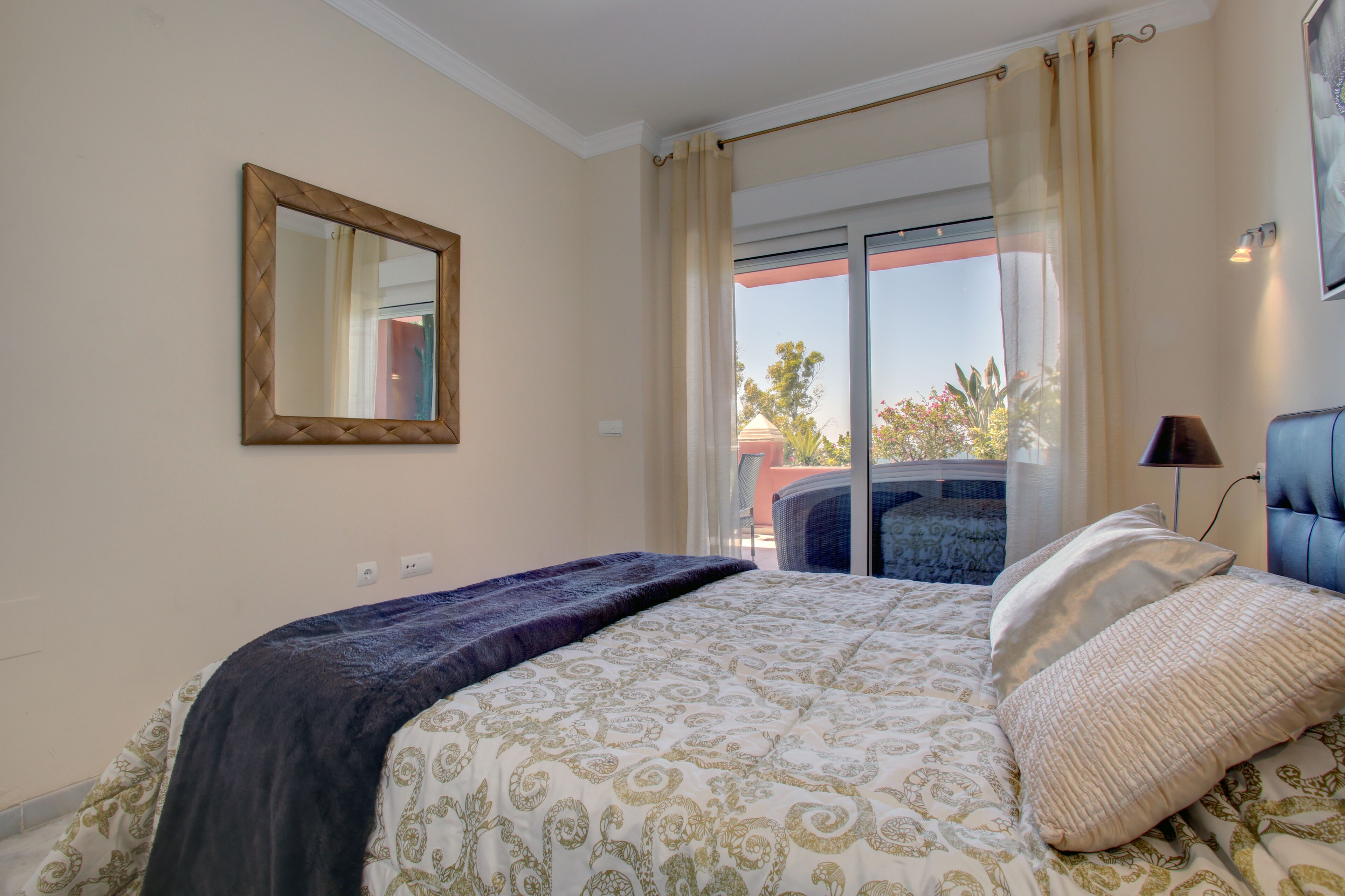 A bedroom with a bed, a large mirror, and a view of the outdoors through a sliding glass door.