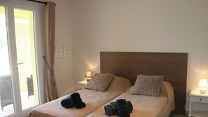 A double bed with two pillows, a nightstand with a lamp, and a sliding glass door with curtains.
