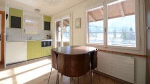 Eine Küche mit Holztisch und -stühlen, einem Fenster mit Blick auf eine verschneite Landschaft und einer Heizung unter dem Fenster.