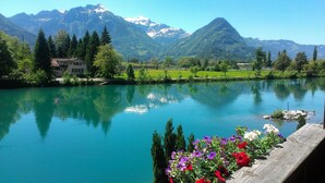 Ein See mit Bergblick, ein Haus und ein Holzsteg mit Blumen.