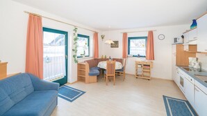 Un espacio habitable compacto con sofá, comedor con mesa y sillas, cocina con estufa y armarios, y ventanas grandes con cortinas.
