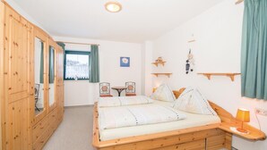 Un dormitorio con una cama de madera, un armario de madera, una mesita pequeña y una silla.