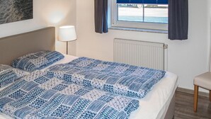 Et hotelværelse med en seng, et natbord, en lampe, et vindue med gardiner og havudsigt.