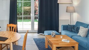En stue med blå sofa, et træbord, et spisebord med stole, og udsigt til en have gennem en glasdør.