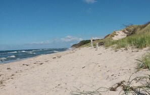 Une plage de sable avec des vagues, un poteau en bois et des dunes herbeuses.