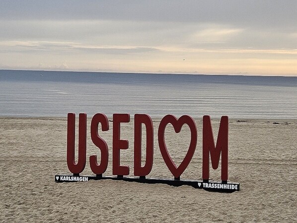 Una playa con letras grandes que deletrean 'USEDOM' y dos ubicaciones: KARLSHAGEN y TRASSENHEIDE.