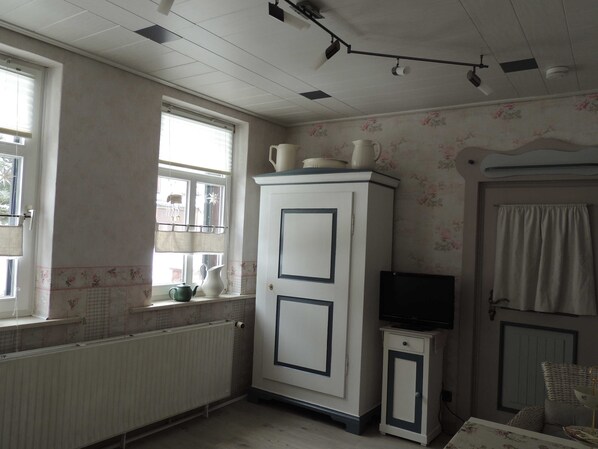 A kitchen with a white cabinet, a small TV, a radiator, and a window with blinds.
