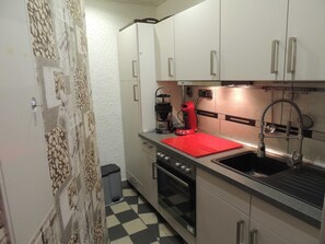 A compact kitchen with a black and white checkered floor, a red countertop, a coffee maker, and a stainless steel sink.