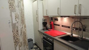 Una cocina compacta con piso a cuadros blancos y negros, una encimera roja, una cafetera y un lavamanos de acero inoxidable.