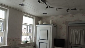 Una cocina con un armario blanco, un televisor pequeño, un radiador y una ventana con persianas.