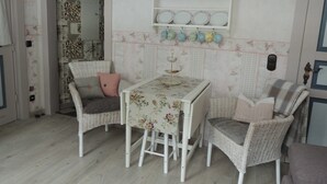 Un comedor con sillas de mimbre, una mesa con mantel floral y un estante con utensilios de cocina.