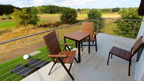 Un balcón con mesa y sillas, vista a un campo de golf y un área verde.