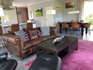 A living room with a brown leather sofa, black and white patterned pillows, a dark coffee table, and a pink carpet.