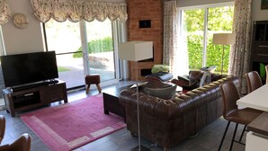 Una sala de estar con un sofá de cuero, un televisor de pantalla plana, una mesa de centro y un comedor con sillas.