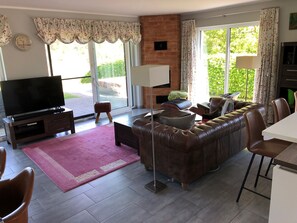 A living room with a leather sofa, a flat-screen TV, a coffee table, and a dining area with chairs.