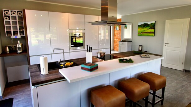 Una cocina moderna con armarios blancos, un horno de acero inoxidable y una isla grande con taburetes.
