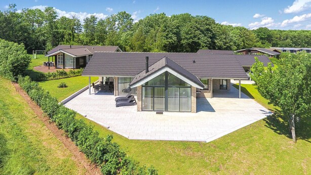 Et moderne hus med stor terrasse, overdækket udeområde og velplejet græsplæne.