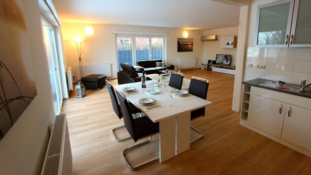 A modern kitchen with white cabinets, a dining table set for four, and a view to the outside. - Villa SEE-RESIDENZ - VILLA SEE-RESIDENZ (Malchow)