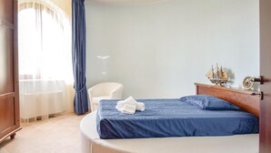 Ein Hotelzimmer mit Bett, Stuhl, Nachttisch aus Holz mit Dekoration und einem Fenster mit Vorhängen.