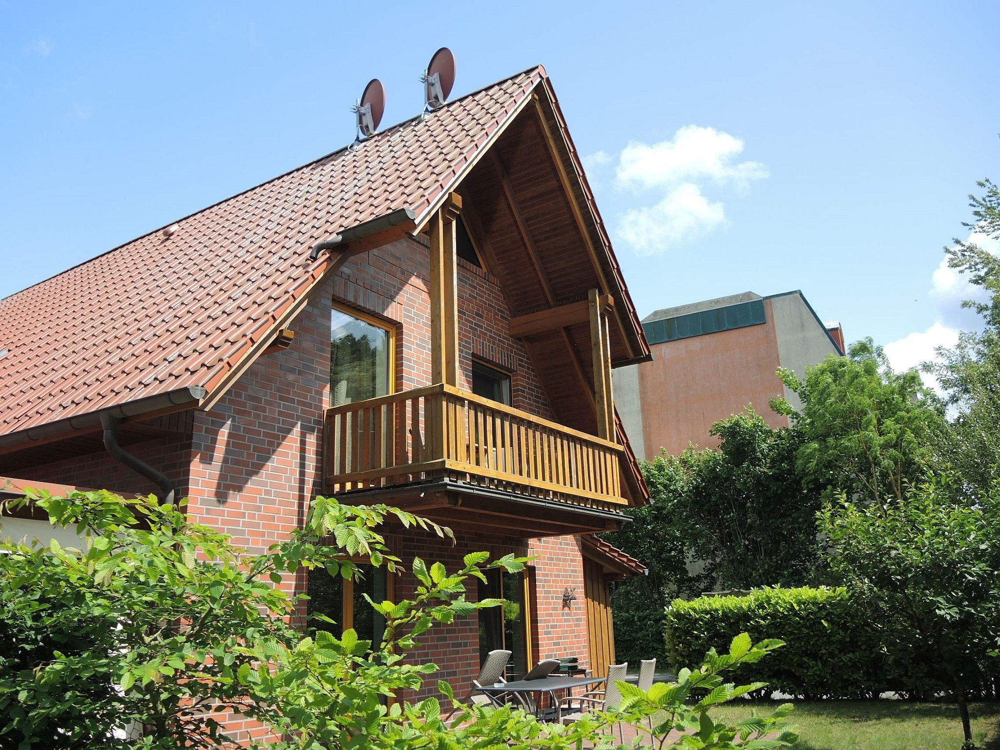 Une maison à deux étages avec une façade en briques, un balcon en bois et une pelouse verdoyante.