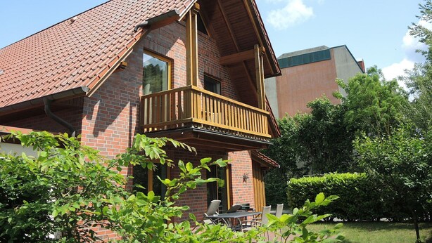 Une maison à deux étages avec une façade en briques, un balcon en bois et une pelouse verdoyante.