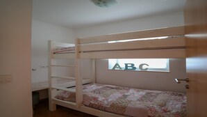 Un lit superposé avec une courtepointe à motifs floraux, une fenêtre ornée des lettres « ABC » et un luminaire au plafond.