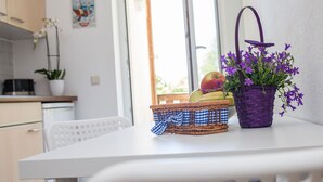 Un coin cuisine avec une table blanche, des paniers en osier et un panier violet contenant des fleurs violettes.