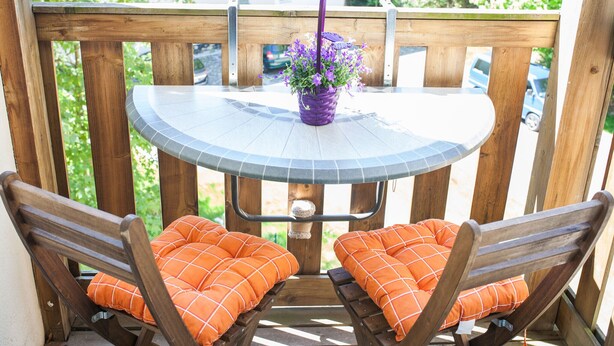 Une terrasse en bois avec une table ronde et deux chaises en bois dotées de coussins orange.