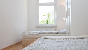 Une chambre à coucher au style minimaliste, avec une grande fenêtre, un lit recouvert d’une literie à motifs et une table de chevet.