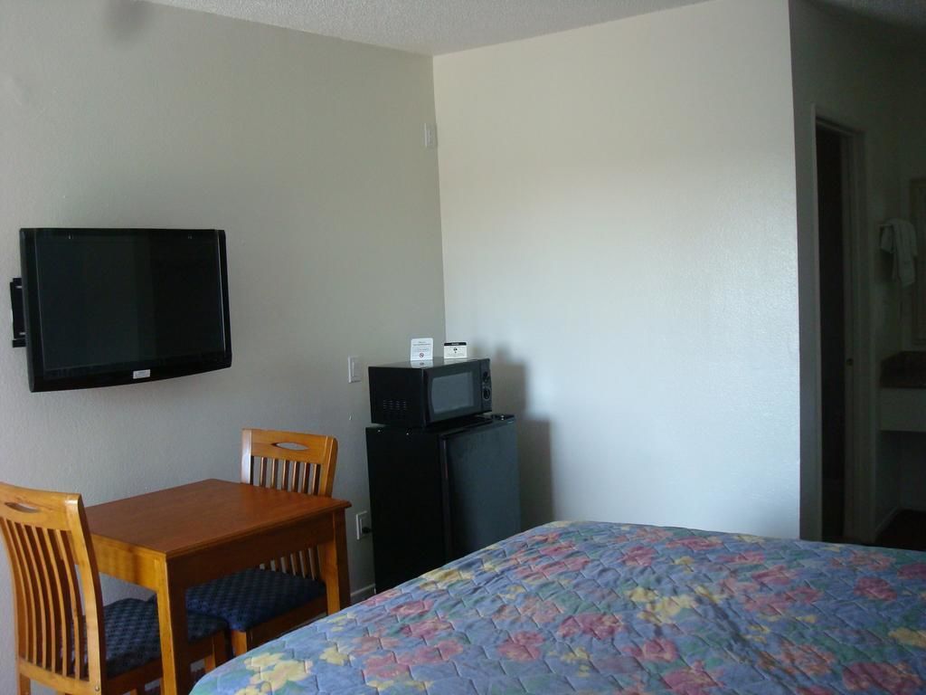 A room with a bed, a TV mounted on the wall, a small table with chairs, and a microwave on a cabinet.