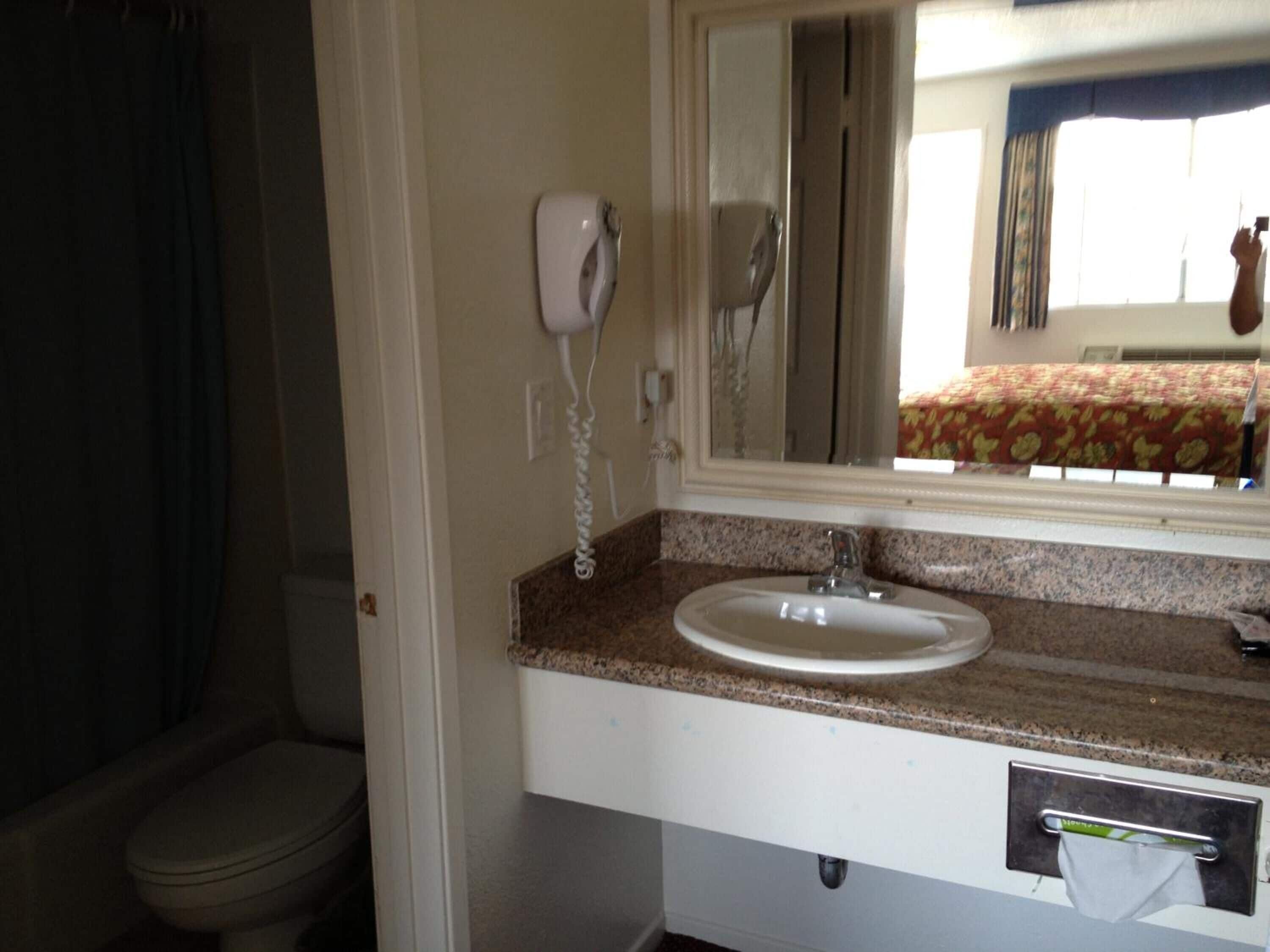 A bathroom with a white sink, a hairdryer mounted on the wall, and a mirror above the sink.