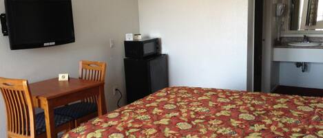 A hotel room with a bed, a desk with a chair, a television, a microwave, and a sink.