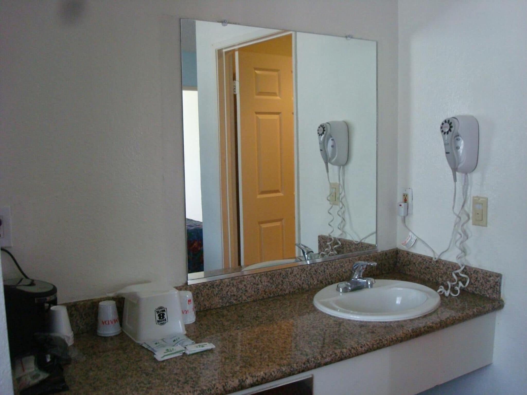Un baño con encimera de granito, un lavabo blanco y dos secadores de pelo montados en la pared.