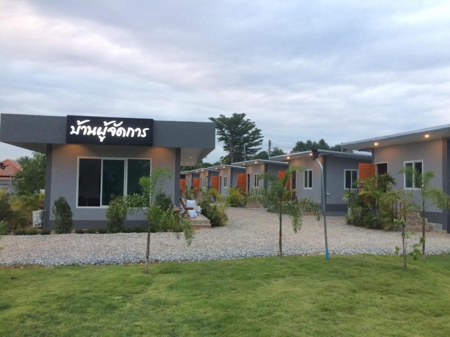 Un hotel moderno con un letrero llamativo, varias habitaciones y un espacio exterior bien cuidado con grava y árboles pequeños.