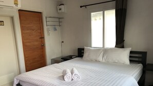 Una cama bien hecha con sábanas y toallas blancas, una puerta de madera, una mesita de noche pequeña y una ventana con cortinas.