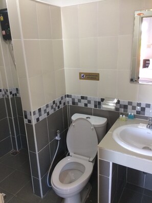Et badeværelse med toilet, bidet og vask. Et skilt på væggen og et spejl over vasken.