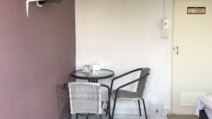 Una habitación pequeña con un televisor montado en la pared, una mesa redonda con dos sillas, una cama y una puerta con un cartel de 'No Fumar'.