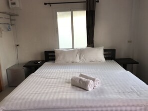 Ein ordentlich bezogenes Bett mit weißen Leinentüchern und zwei Kissen, ein Nachttisch mit Fernbedienung und ein Fenster mit Vorhängen.