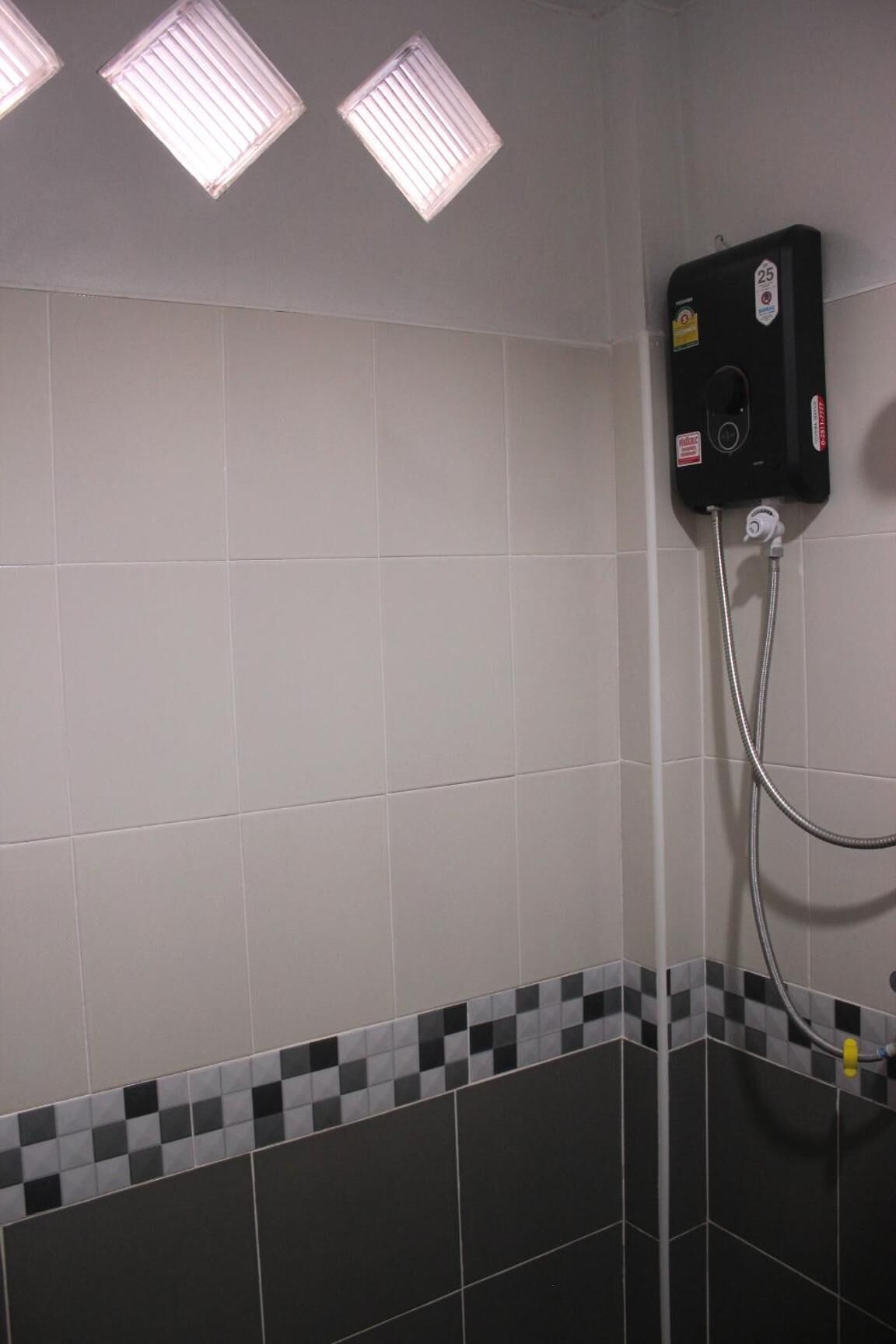 A bathroom with white tiled walls, a black and white checkered border at the bottom, and a shower unit with a hose.