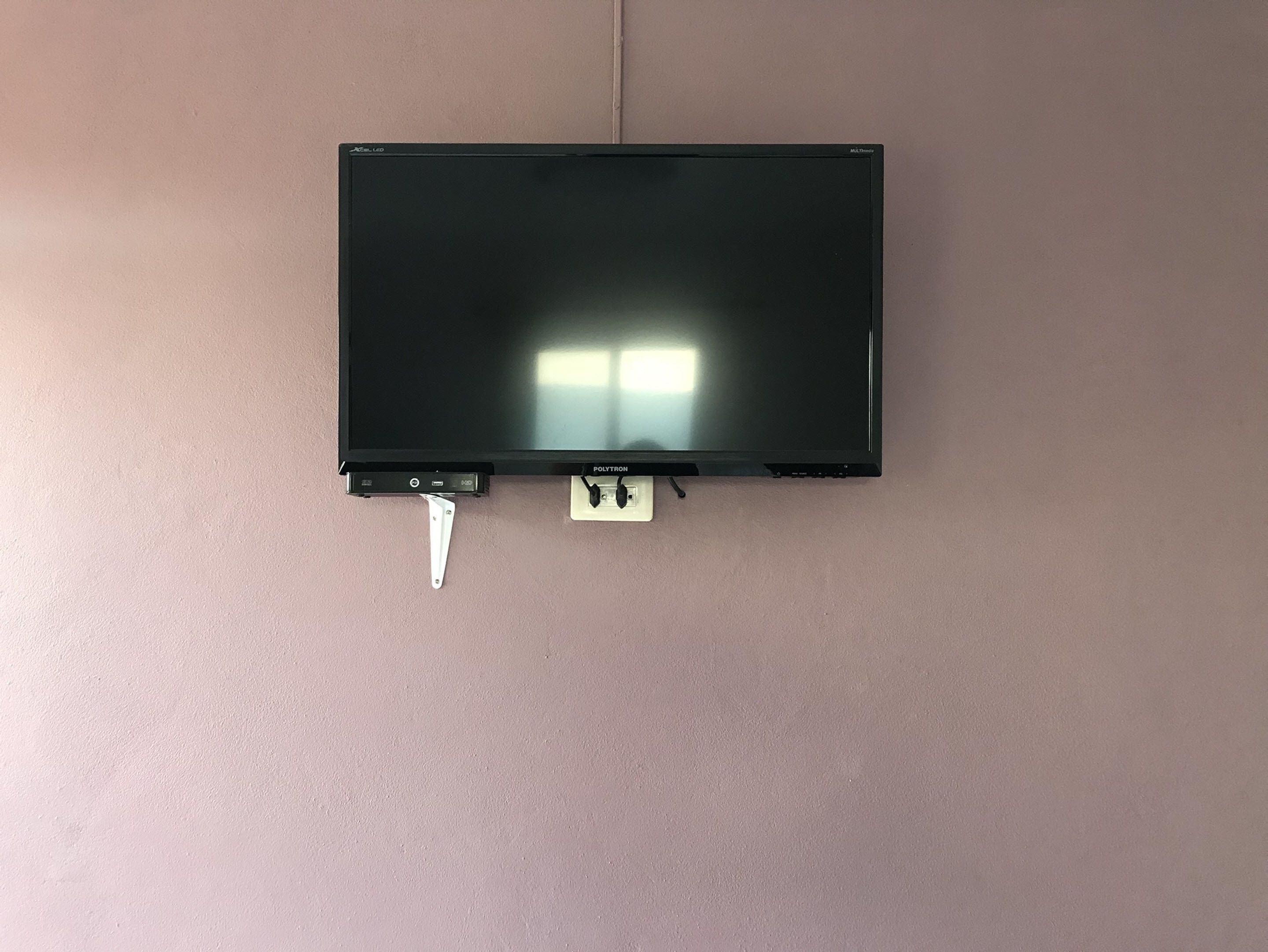 A black flat-screen TV mounted on a wall with a white power cord and a power outlet below it.