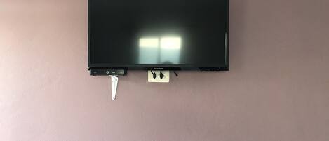 A black flat-screen TV mounted on a wall with a white power cord and a power outlet below it.