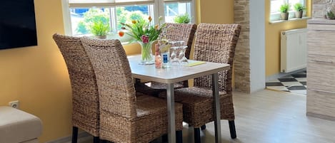 Un comedor con sillas de mimbre, una mesa con un florero y una ventana con persianas.