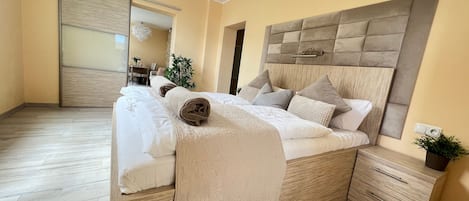 A bedroom with a large bed, a wooden headboard, a bedside table, and a small drawer unit.