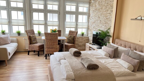 Une chambre d’hôtel avec un grand lit, une table à manger avec des chaises, une télévision et un mur en pierre.