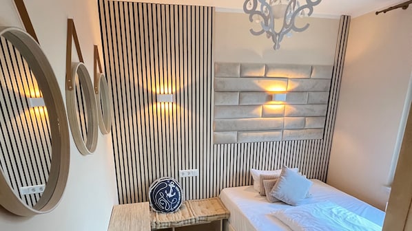 A bedroom with a bed, a bedside table, a decorative wall panel, and a wall-mounted light fixture.