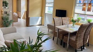 Un salon moderne avec un canapé, une table à manger, des chaises en osier, un téléviseur et des plantes en pot.